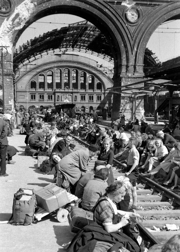 A large group of people, adults and children, sit on the edge of the train tracks near the Brandenberg Gate, Berlin, Germany, August 1945. (Photo by Margaret Bourke White/ © Time & Life Pictures/Getty Images)